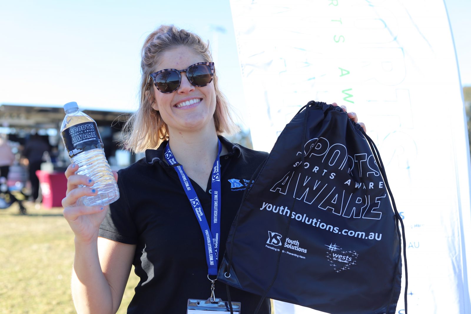 Youth Solutions Manager Emily Deans holds up a Sports AWARE drink bottle and drawstring bag outside at a Sports AWARE outreach activity.